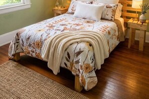 Ein Bett mit floralem Überwurf, ein Nachttisch mit Lampe und ein Holzboden.