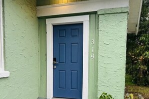 Eine blaue Tür mit weißem Rahmen, Hausnummer 310, und eine grüne Wand mit Struktur.
