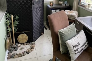A room with a chair, a cushion with text, a small table with items, and a decorative arrangement of stones and plants. - Cozy 2-bedroom bungalow with AC in charming Jacksonville (Jacksonville)