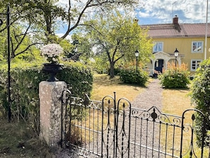 Une entrée fermée par un portail donne accès à une propriété, un chemin mène à un bâtiment dont le toit est recouvert de tuiles.