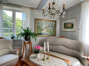 Quarto com sofá, mesa com um vaso de flores, luminária de cristal e duas quadros na parede.