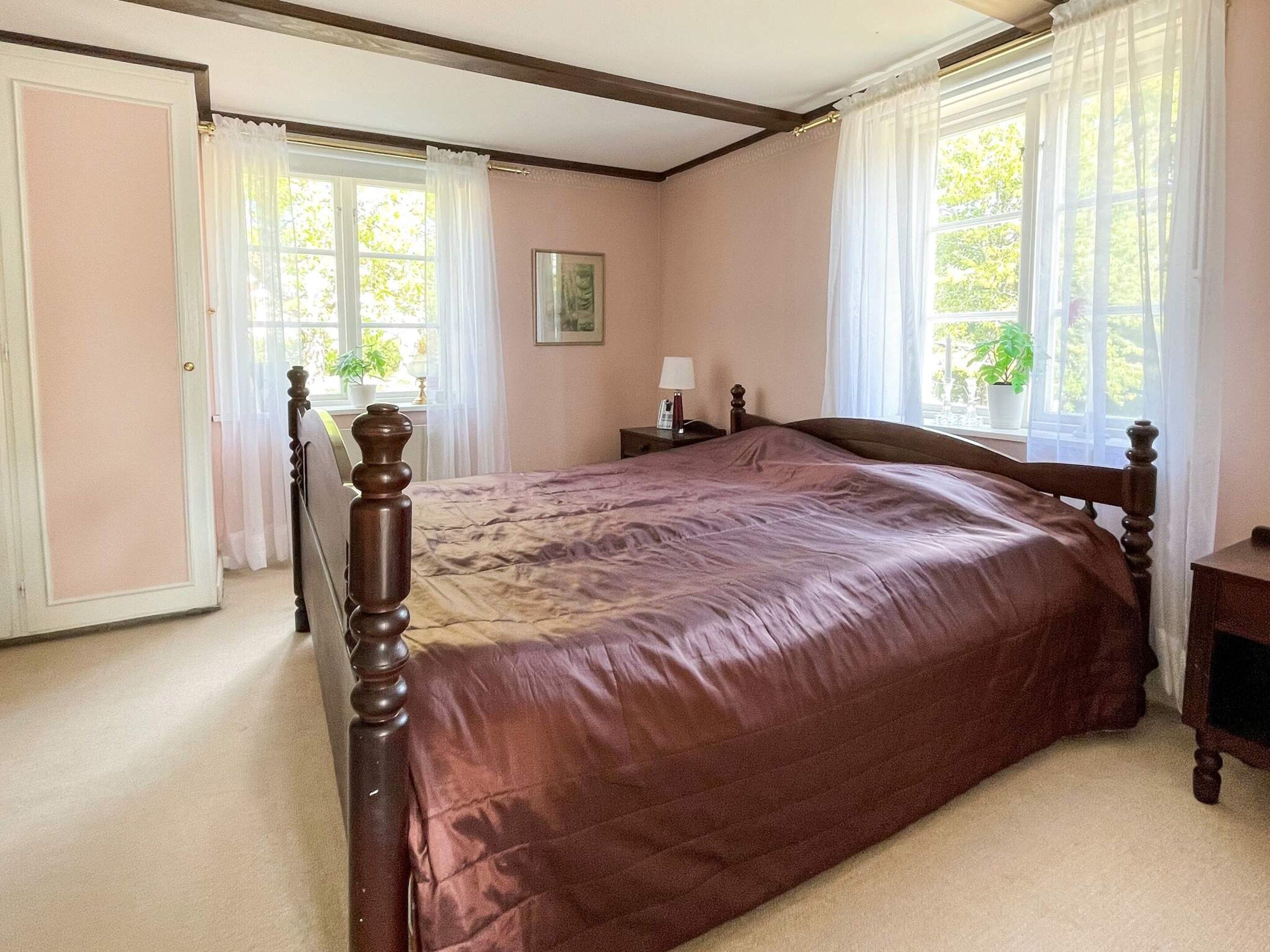 A bedroom with a large bed, two bedside tables, a nightstand, a window with curtains, and a door.