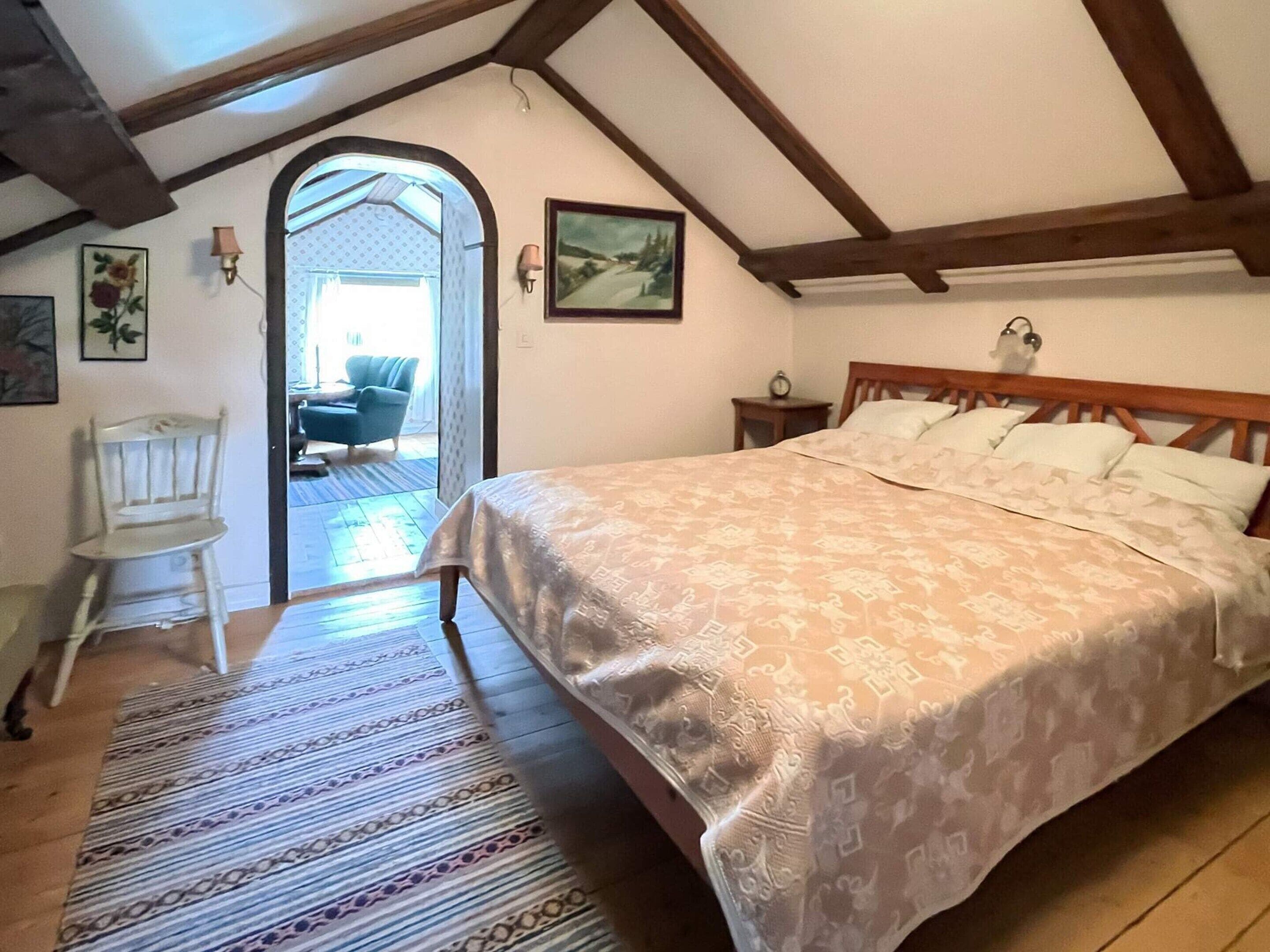 A bedroom with a bed, a chair, a rug, and a painting on the wall.
