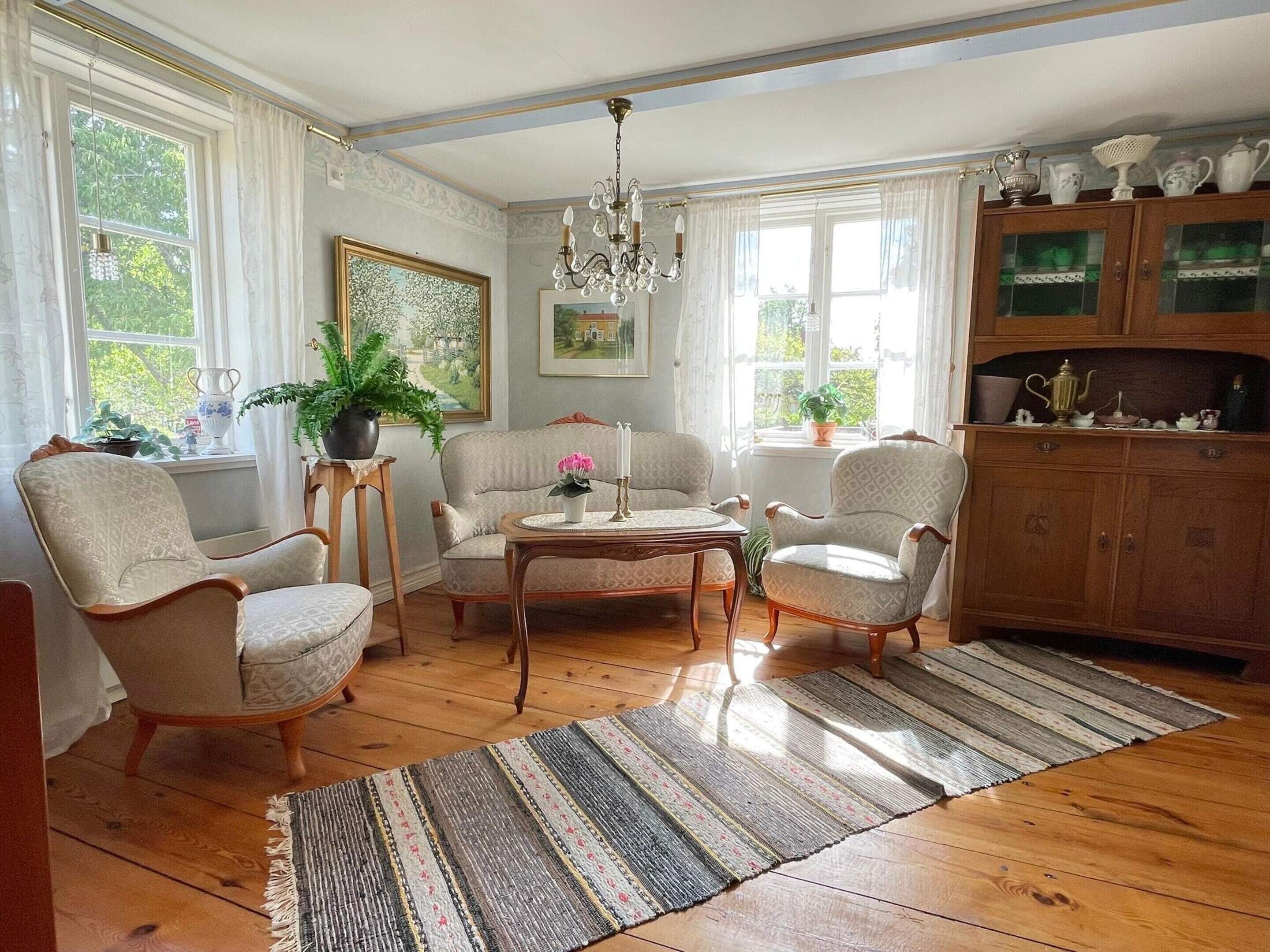 A well-lit living room with a chandelier, wooden furniture, a rug, and a cabinet with decorative items.