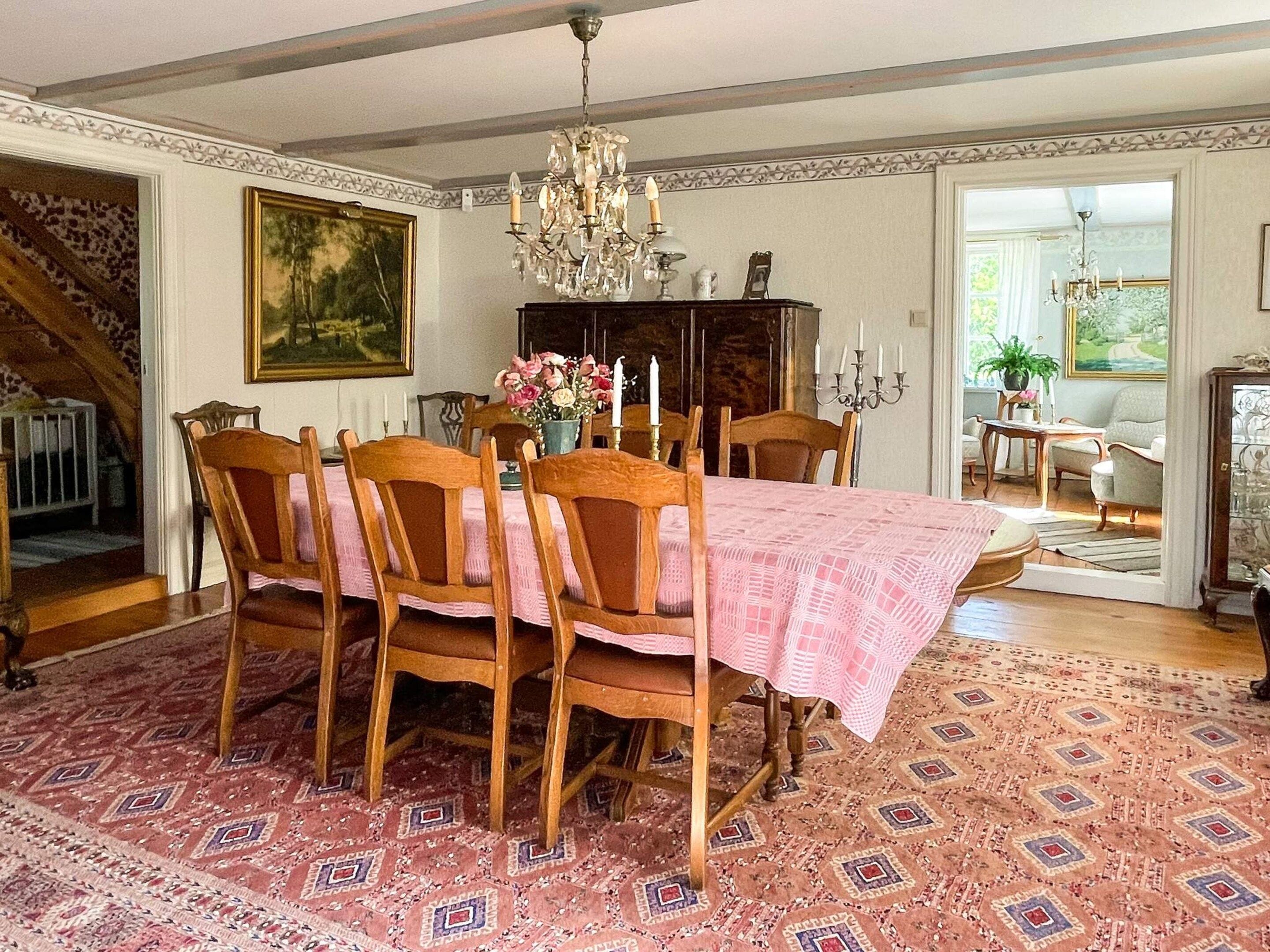 Comedor con una mesa dispuesta para seis personas, rodeada de sillas de madera, una araña y una alfombra estampada.