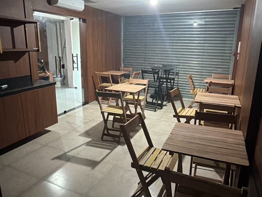 Una habitación amplia con zona de cocina, varias mesas y sillas de madera, y un techo con diseño lineal.