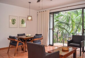A dining area with a wooden table and chairs, a ceiling fan, and a view of a tropical garden through a glass door. - Central Apartment in the Hotel Zone, 10 Minutes from the Boardwalk (Puerto Vallarta)