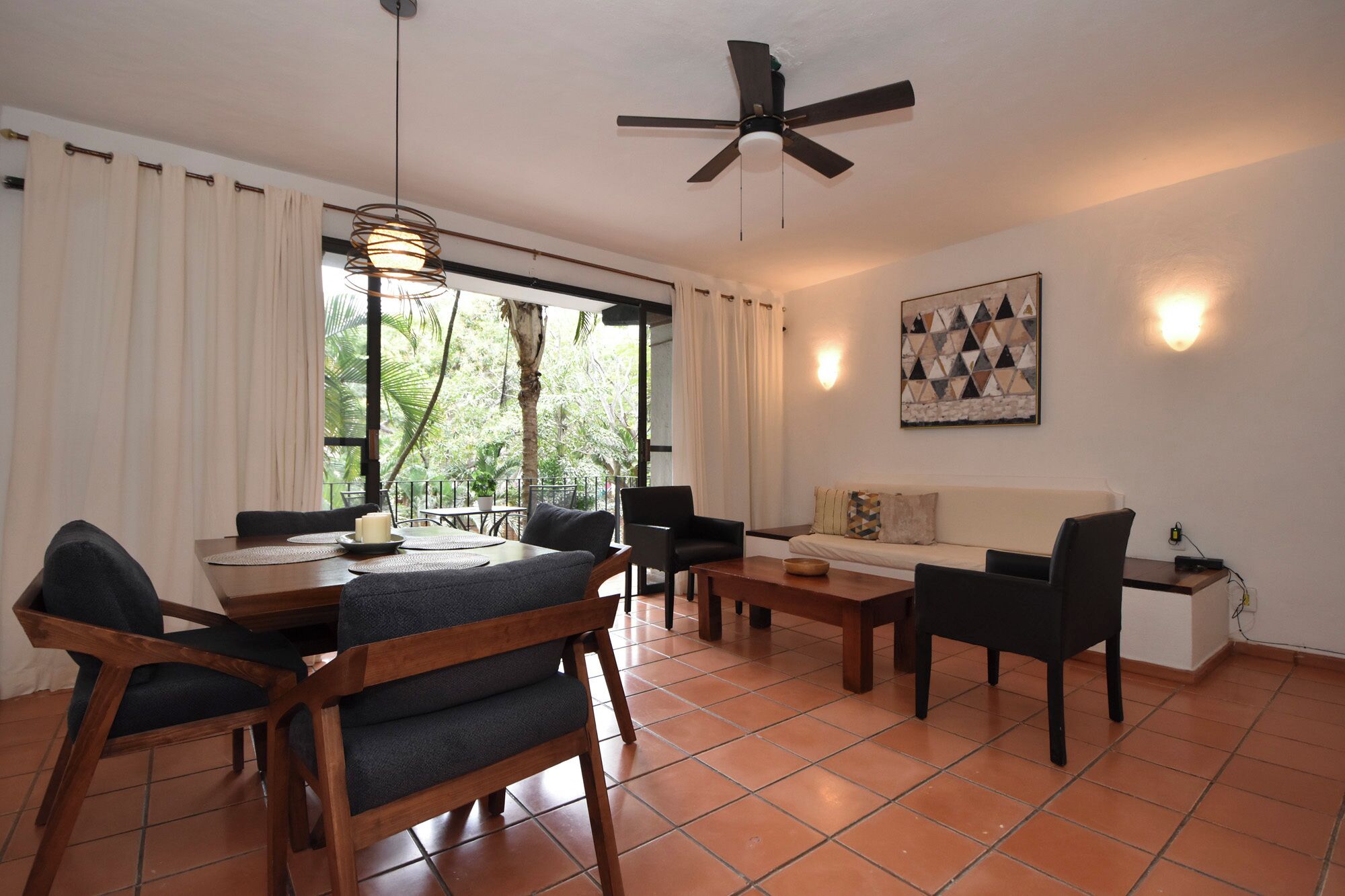 A living room with a sofa, chairs, a dining table, and a ceiling fan.
