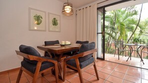 Comedor con una mesa y sillas de madera, una lámpara colgante y vistas a palmeras a través de un ventanal.