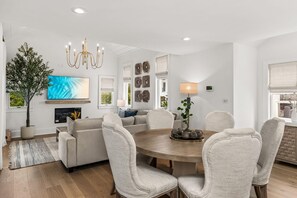 Una sala de estar moderna con una mesa redonda de madera, sofás color beige y un televisor de pantalla plana grande.