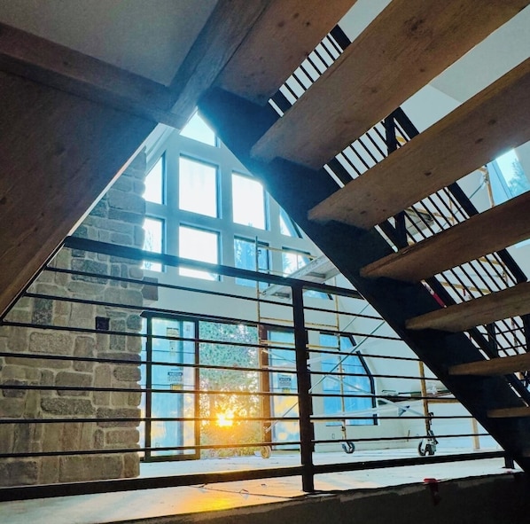 A high-ceilinged room with a wooden staircase and large windows.