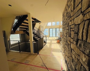 A multi-level interior with a staircase, stone wall, and large windows.