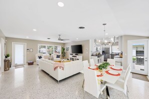 A modern kitchen with stainless steel appliances, a dining area with white furniture, and a living room with a white sofa and a flat-screen TV. - 4-Min Walk to Atlantic Ave | Hot Tub, Sleeps 6 (Delray Beach)