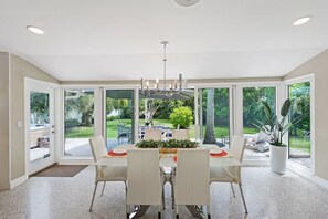 A dining area with a table set for four, surrounded by large windows offering a view of a garden and outdoor seating. - 4-Min Walk to Atlantic Ave | Hot Tub, Sleeps 6 (Delray Beach)