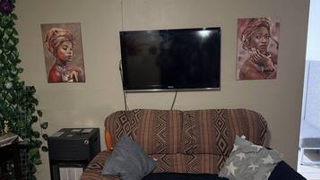 Una sala de estar con un sofá estampado, un televisor de pantalla plana y dos cuadros colgados en la pared.