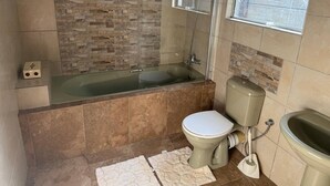 Un baño con bañera de hidromasaje con mampara de vidrio, inodoro y bidé.
