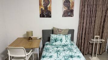 A room with a bed, a desk, a chair, and two wall-mounted paintings.