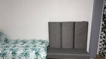 Una habitació amb un llit, una banca tapissada de gris i un paviment de rajoles.