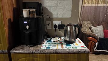 A kitchen counter with a coffee maker, a kettle, and a microwave. There is a wooden cabinet below the counter.