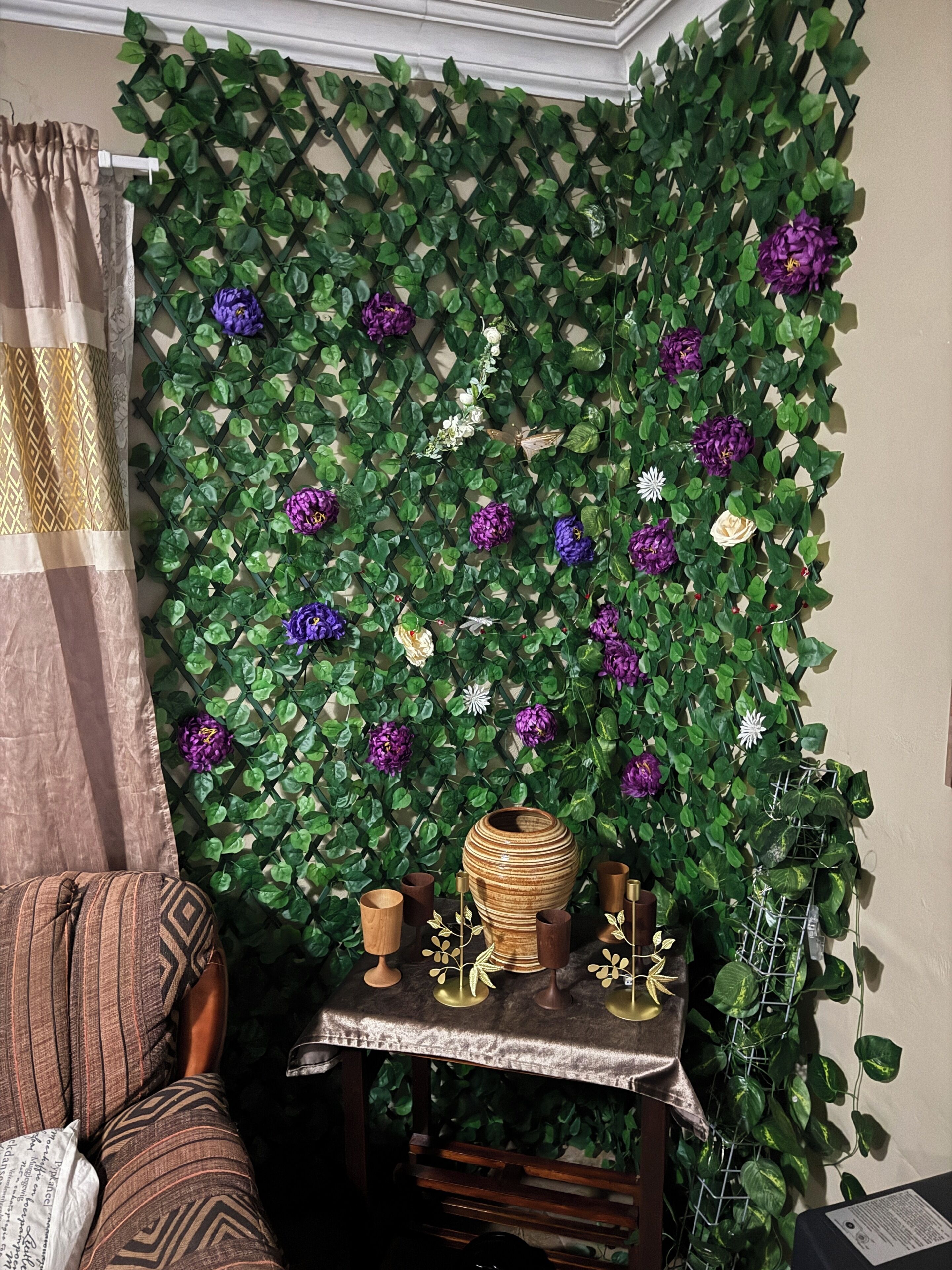 A room with a green leafy wall, a patterned curtain, a cushioned sofa, and a small table with decorative items.