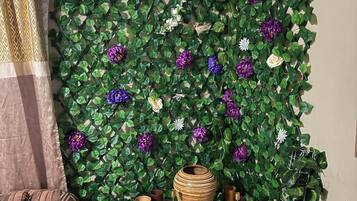 A room with a green leafy wall, a patterned curtain, a cushioned sofa, and a small table with decorative items.