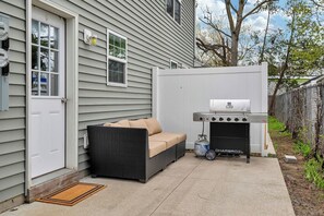 A patio with a grill and a wicker sofa.