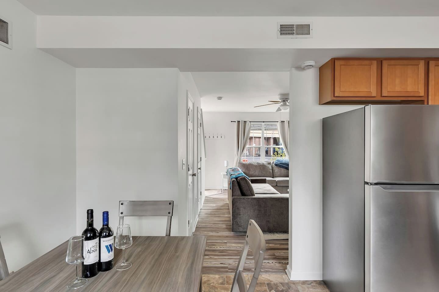 A modern kitchen with a stainless steel refrigerator, a dining area with a table and chairs, and a view into the living room.