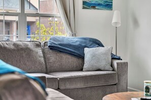 A grey sofa with a blue blanket and a patterned pillow, a floor lamp, and a painting of a ship on the wall.