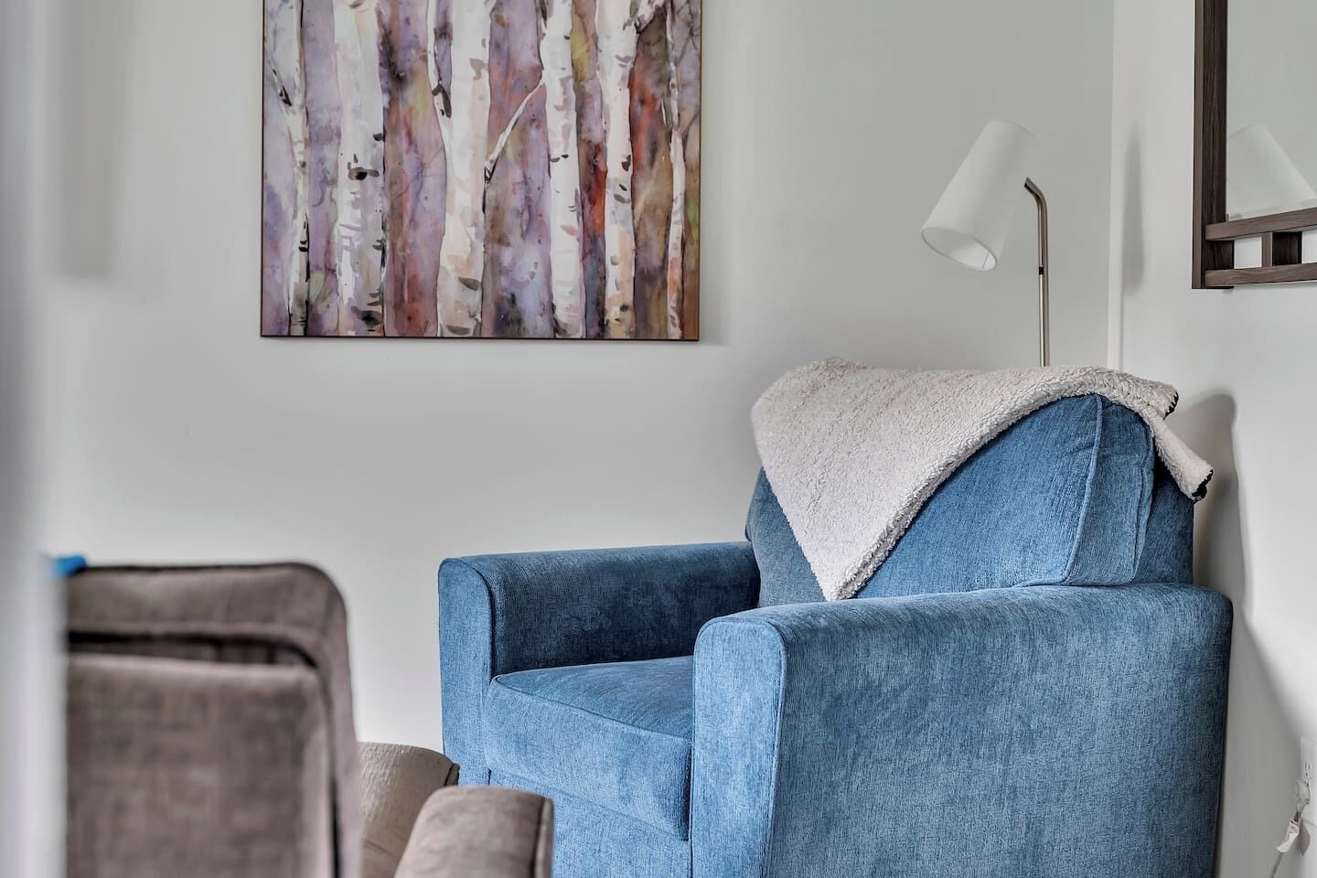 Et værelse med en blå lænestol, en hvid lampe og et billede på væggen.