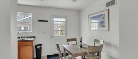 A compact dining area with a wooden table and chairs, a window with a view, and a kitchen with a sink and cabinets.