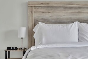 A neatly made bed with white linens, a bedside lamp, and a digital clock on a bedside table.