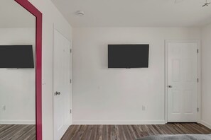 A room with a flat-screen TV mounted on the wall, a white door, and a wooden floor.