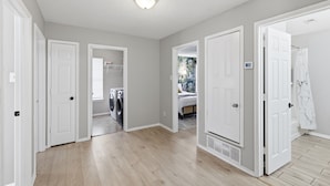 A hallway with white doors leading to various rooms, a laundry area with washing machines, and a thermostat on the wall.