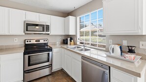 A modern kitchen with white cabinetry, a stainless steel stove, a microwave, and a dishwasher.