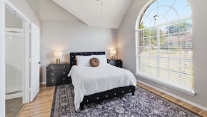 A bedroom with a bed, two bedside tables, a ceiling fan, and a large window with blinds.