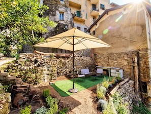 An outdoor seating area with a table and chairs under a canopy, surrounded by a stone wall and greenery. - Charming vacation home with a garden, balcony, and a magnificent view! (Ceriana)