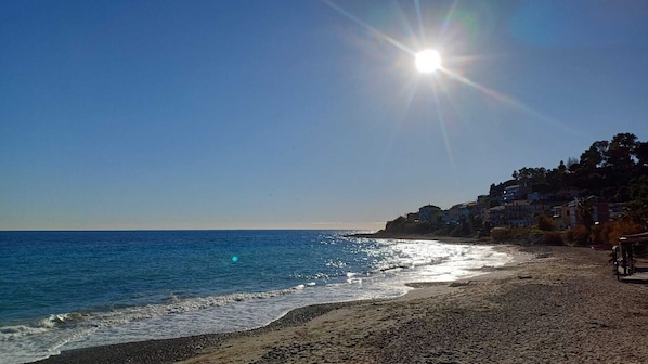 Ein Strand mit blauem Himmel, strahlender Sonne und Gebäuden auf der rechten Seite.