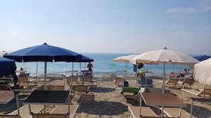 A beach with rows of sun loungers and umbrellas, some occupied, others empty, under a clear sky. - Charming vacation home with a garden, balcony, and a magnificent view! (Ceriana)