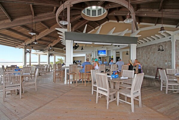 An outdoor dining area with wooden furniture and a view of the ocean. - Anchor Down - 2 Bed | Beach, Fun, Dining, Golf (Seabrook Island)