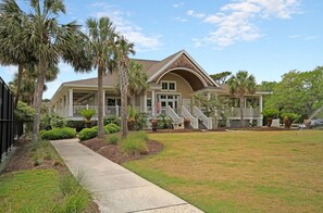 A two-story house with a covered porch, a front yard with grass and palm trees, and a driveway leading to the entrance. - Anchor Down - 2 Bed | Beach, Fun, Dining, Golf (Seabrook Island)