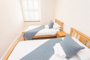 A room with two single beds, each with a wooden headboard, white bedding, and a blue knitted throw. There is a small wooden nightstand beside each bed. - Derby Cottage, Ambleside a popular dog friendly and centrally located cottage (Ambleside)
