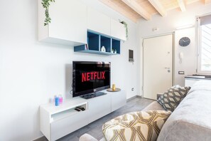 Een moderne slaapkamer met een flatscreen-tv waarop 'NETFLIX' staat, een witte console, een bed met beddengoed met een patroon en een deur met een klok.
