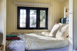 A bedroom with a large bed, a window with black shutters, and a wooden headboard.