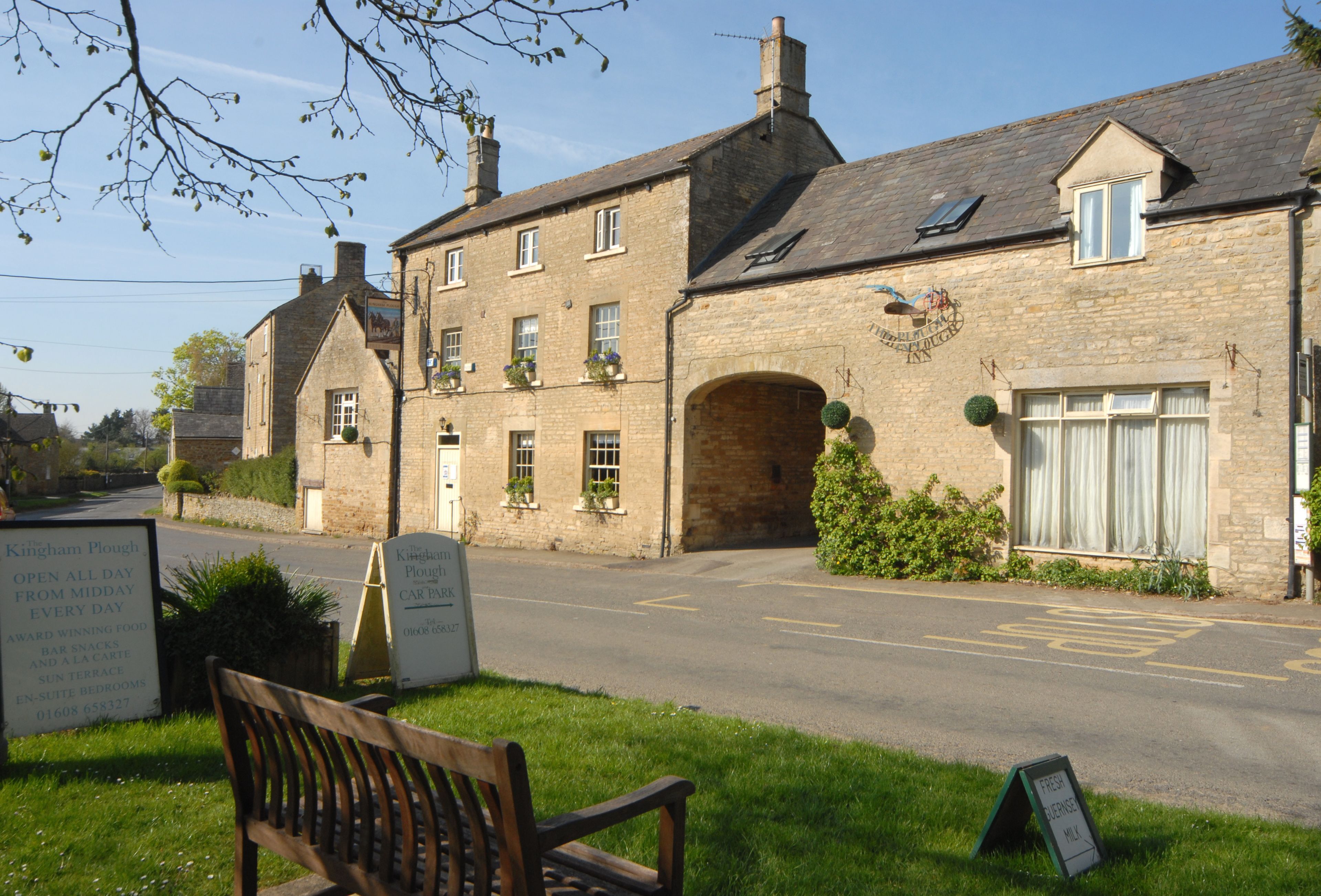 Un bâtiment en pierre avec une enseigne, un banc et une route dégagée devant.