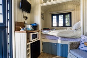A compact room with a bed, a small kitchenette, a television, and a window.