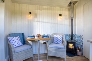 A cozy outdoor seating area with wicker chairs, a wooden table, and a black wood stove.