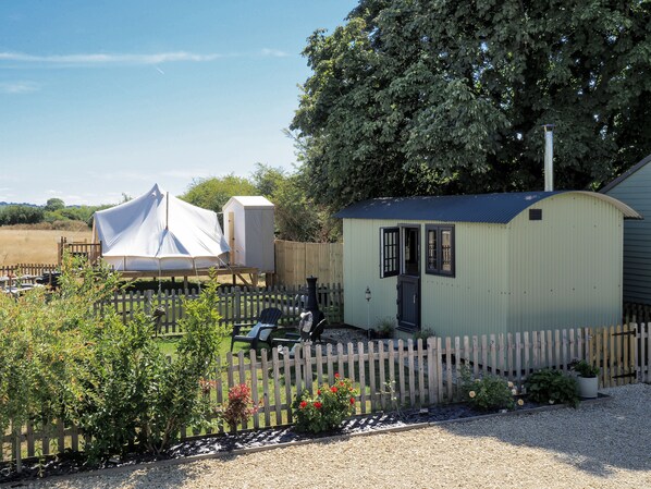 A small, single-story building with a door and windows, surrounded by a wooden fence, and a tent set up nearby.