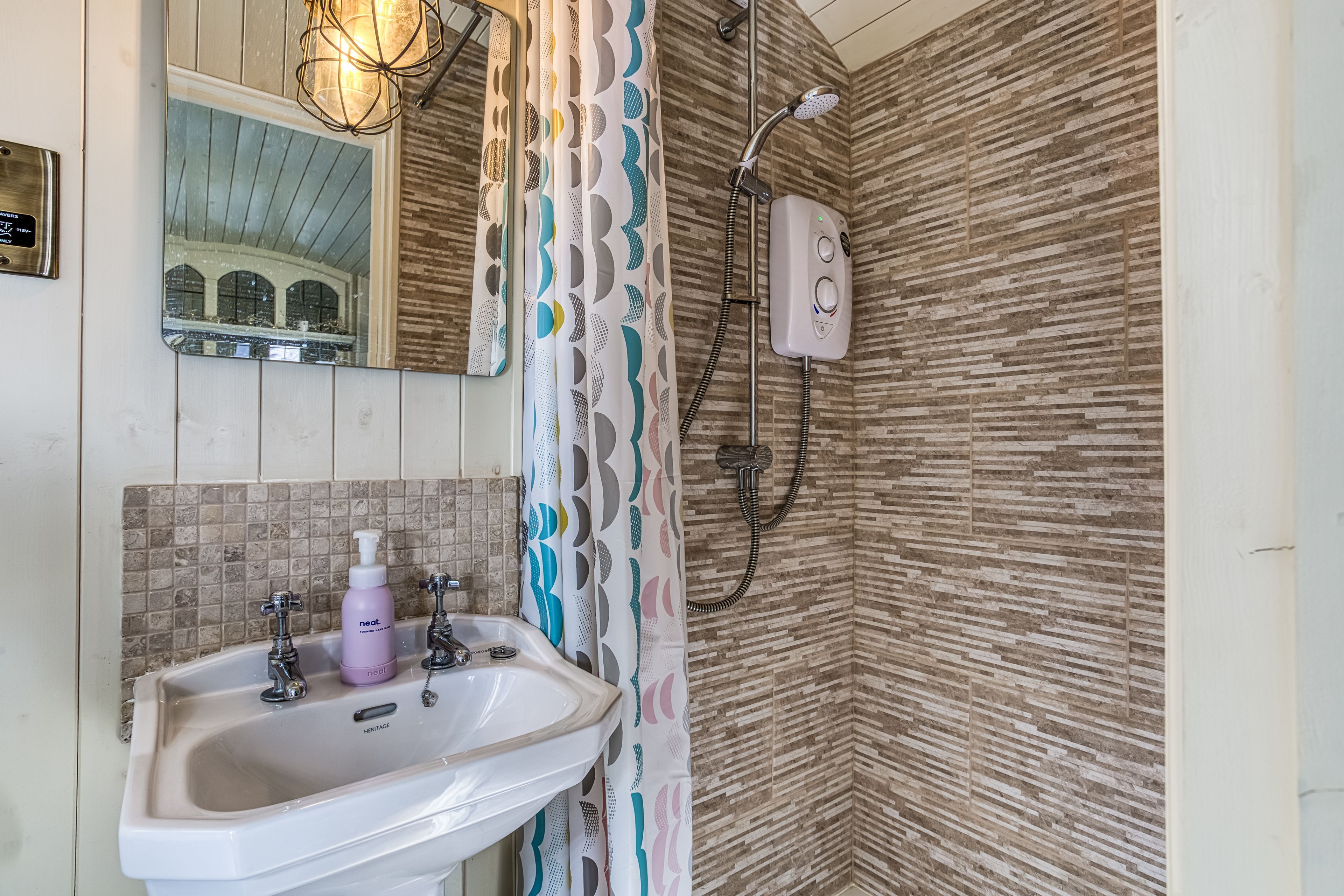 Une salle de bain équipée d’un lavabo, d’un miroir, d’une douche et d’un rideau de douche à motifs.