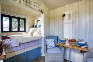 A room with a bed, a table with bowls and a mug, and a chair.