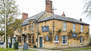 Un edificio histórico con un letrero que indica el pub “The Swan”, fachada de piedra tradicional y un letrero que señala “Bourton Road”.